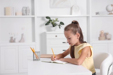 Photo of Girl with correct posture doing homework at white desk indoors