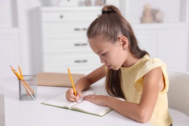 Girl with incorrect posture doing homework at white desk indoors