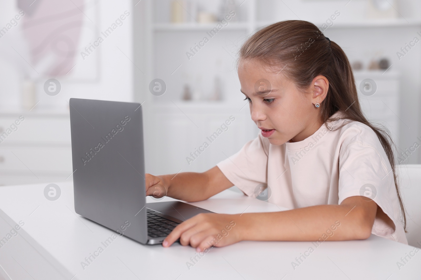 Photo of Girl with incorrect posture using laptop at white desk indoors