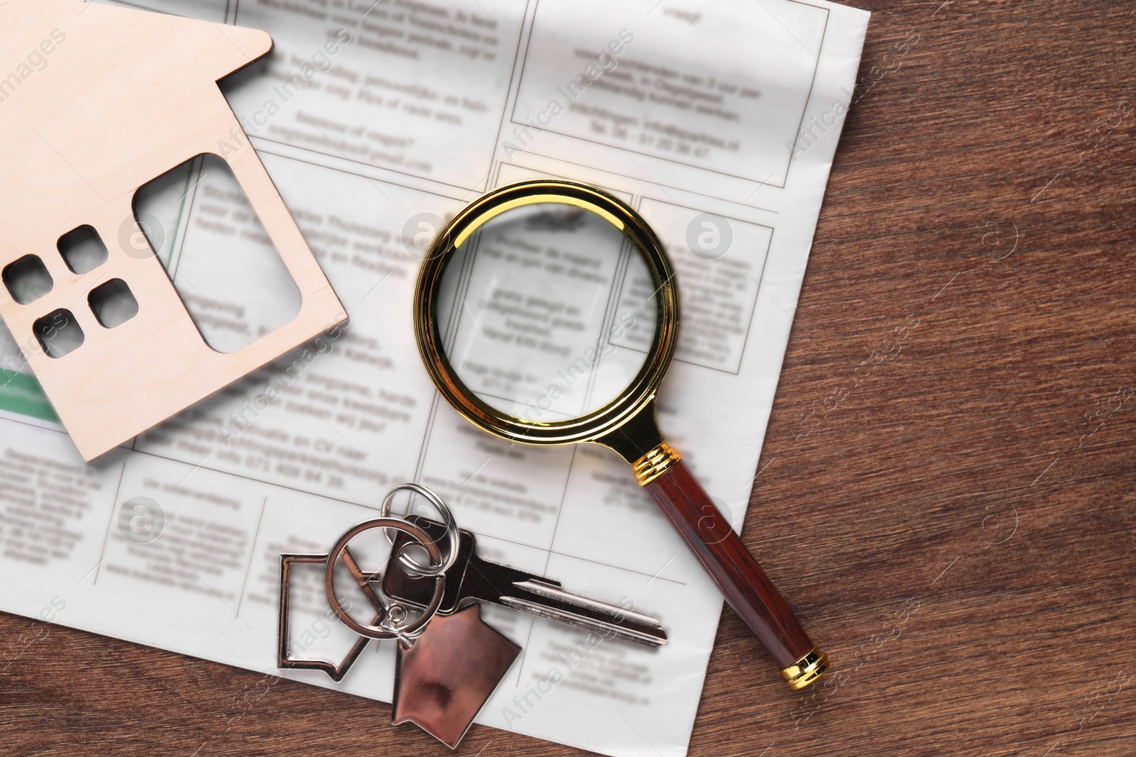 Photo of House hunting. Magnifying glass, keys, house figure and newspaper on wooden table, flat lay