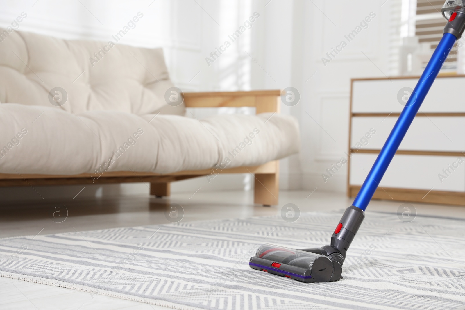 Photo of Cleaning carpet with cordless vacuum cleaner indoors, closeup. Space for text