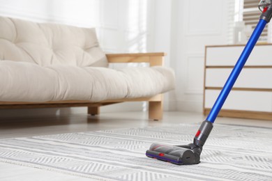 Photo of Cleaning carpet with cordless vacuum cleaner indoors, closeup. Space for text