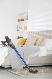 Photo of One cordless vacuum cleaner leaning on bed indoors