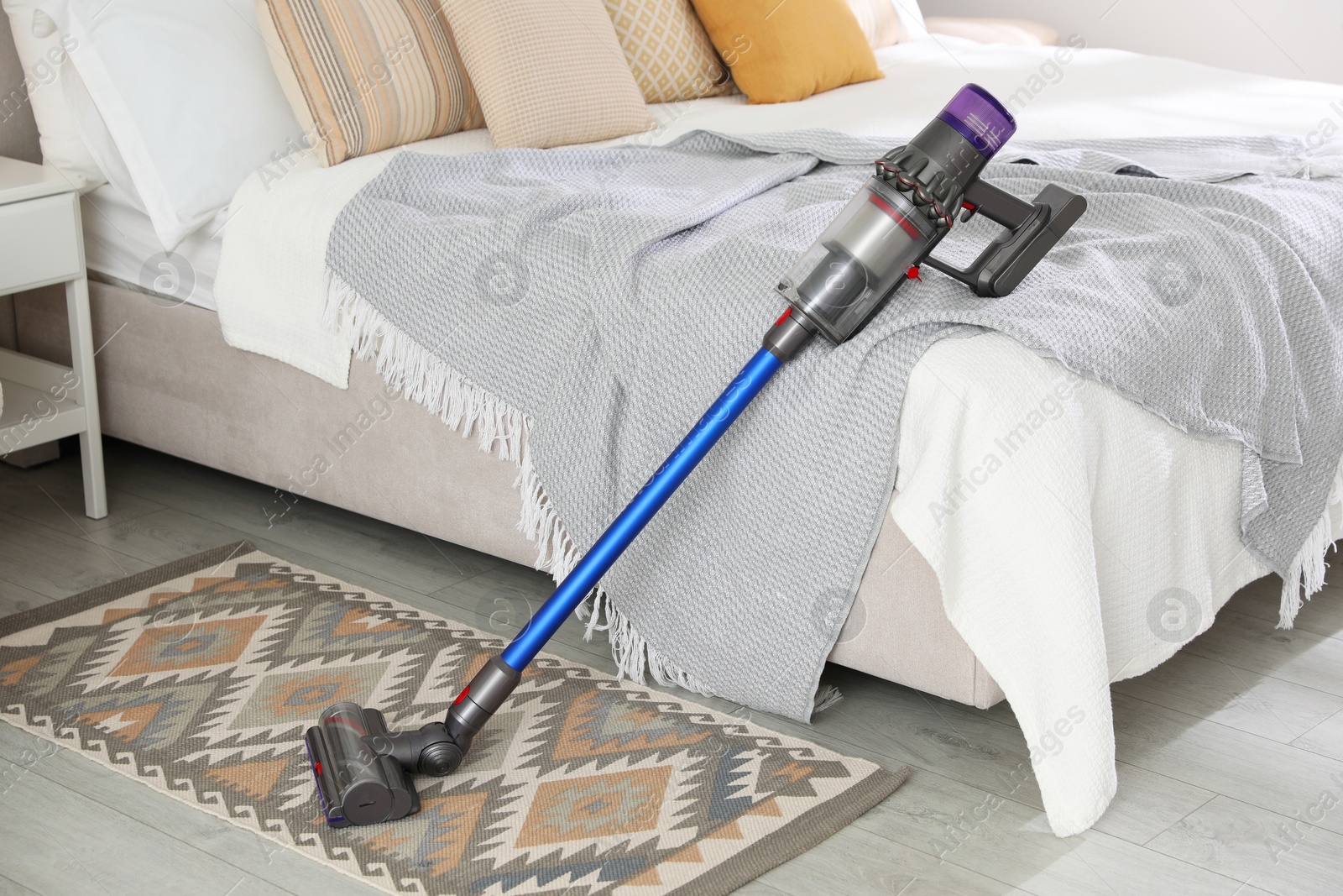 Photo of One cordless vacuum cleaner leaning on bed indoors