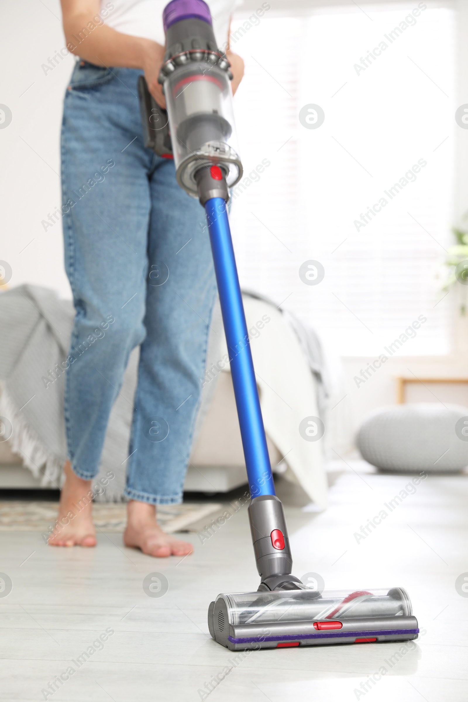 Photo of Woman cleaning floor with cordless vacuum cleaner indoors, closeup