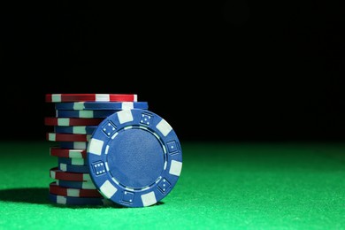 Photo of Poker chips on green table against dark background, closeup. Space for text