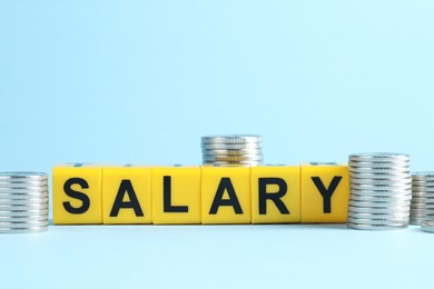 Photo of Word Salary made of cubes and coins on light blue background