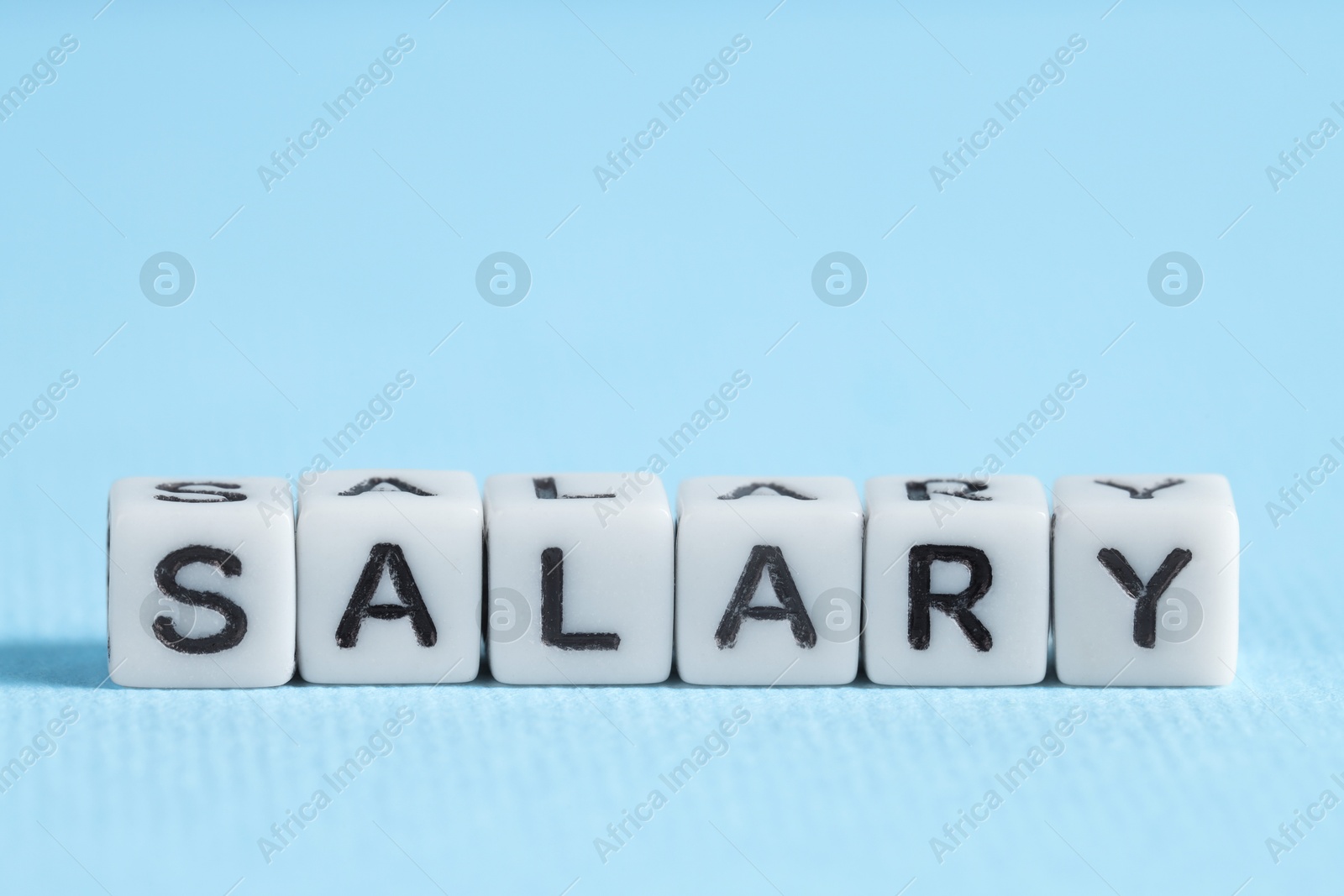 Photo of Word Salary made of cubes on light blue background