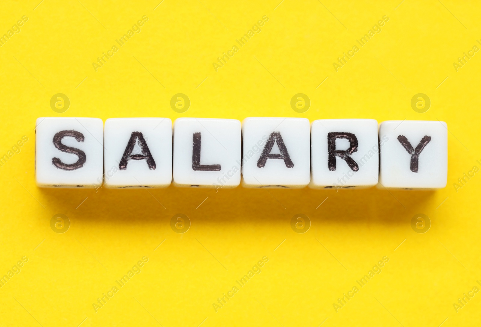 Photo of Word Salary made of cubes on yellow background, top view