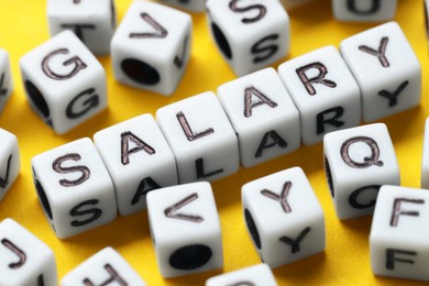 Photo of Word Salary made of cubes on yellow background, closeup