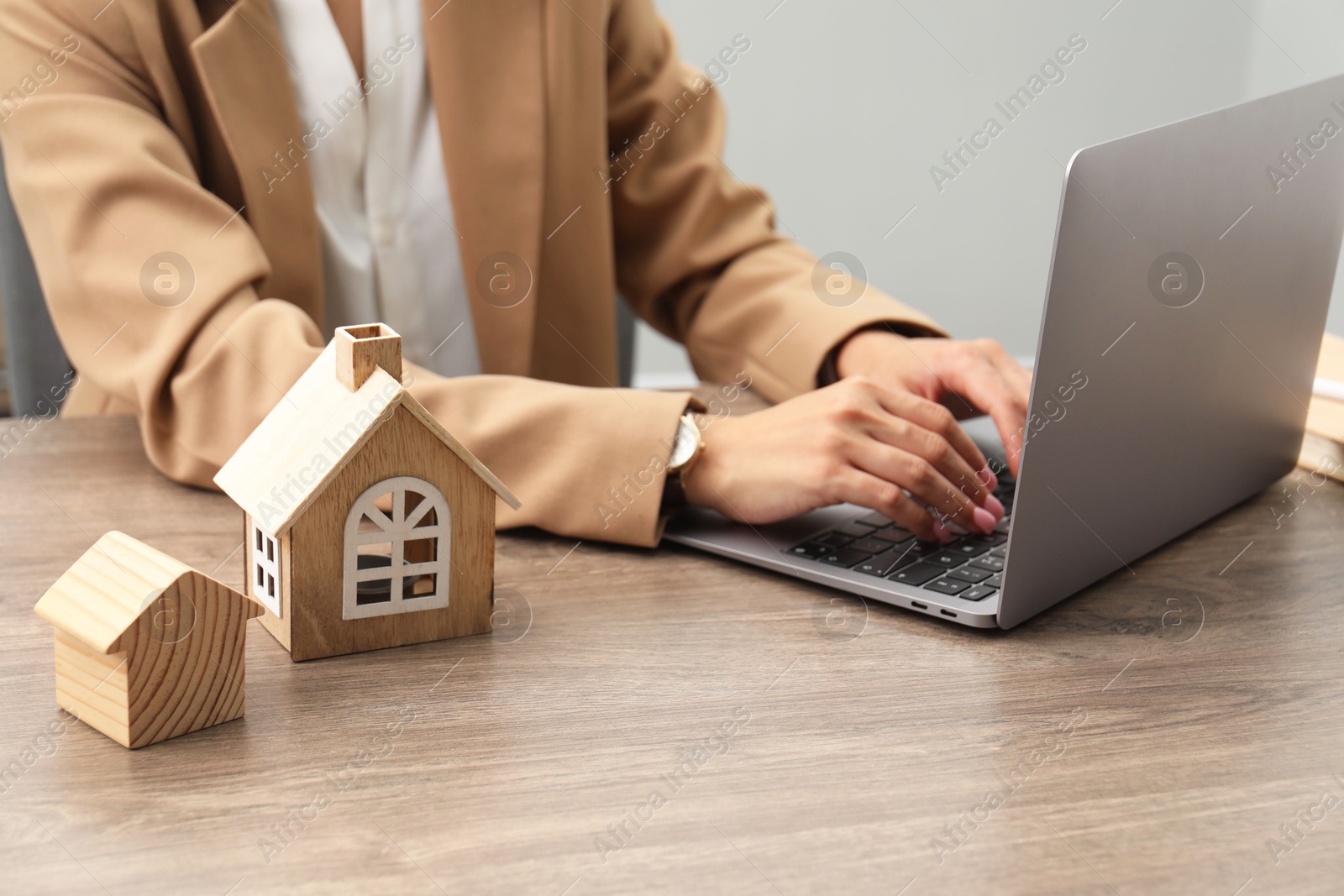 Photo of House hunting. Woman with laptop and house figures at wooden table, closeup