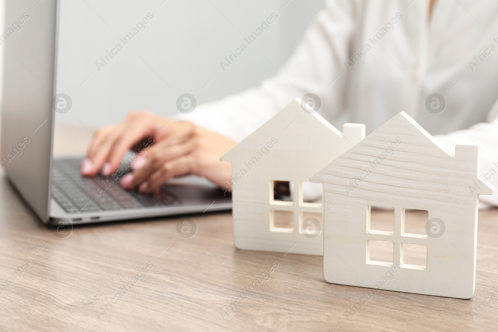 Photo of House hunting. Woman with laptop and house figures at wooden table, closeup