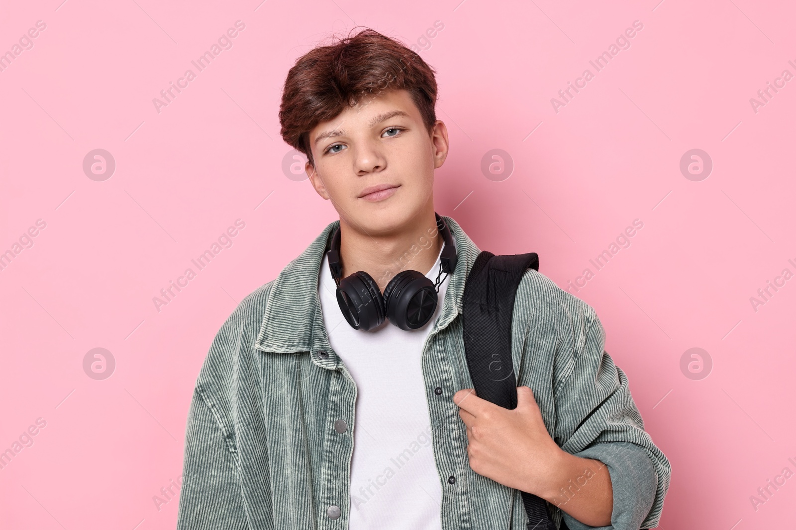 Photo of Teenage boy with headphones and backpack on pink background