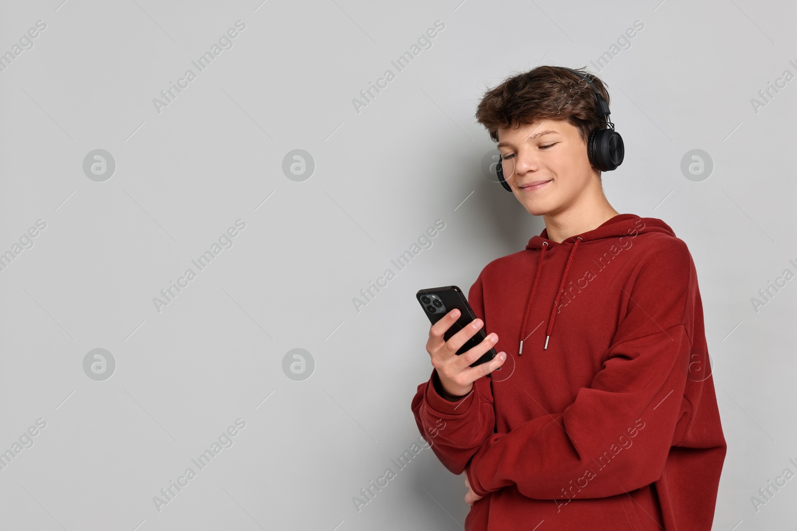 Photo of Teenage boy in headphones with smartphone on light grey background, space for text