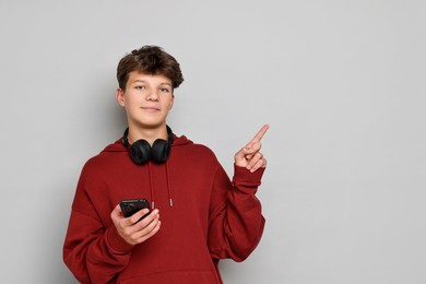 Photo of Teenage boy with headphones and smartphone on light grey background, space for text