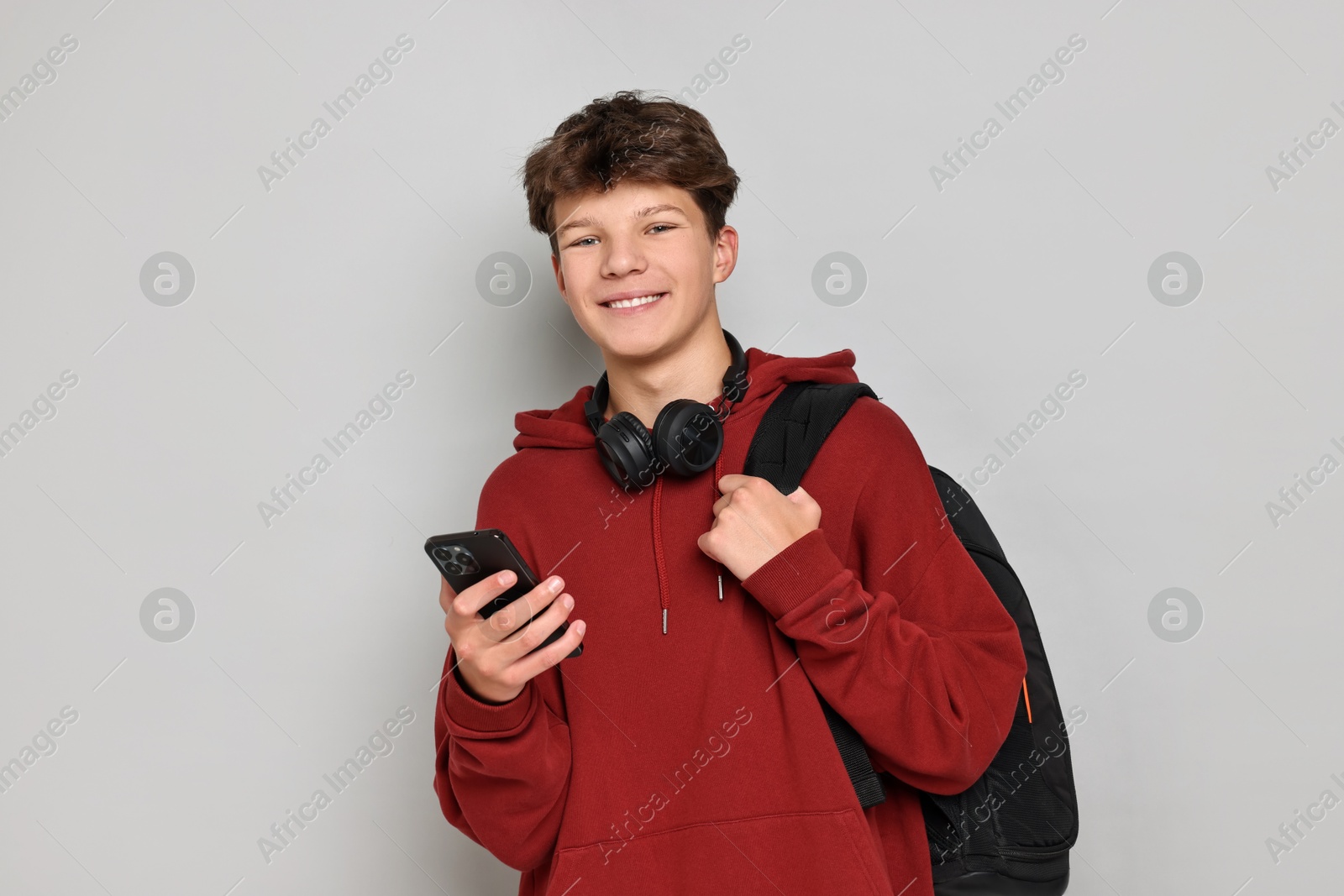 Photo of Teenage boy with headphones, smartphone and backpack on light grey background