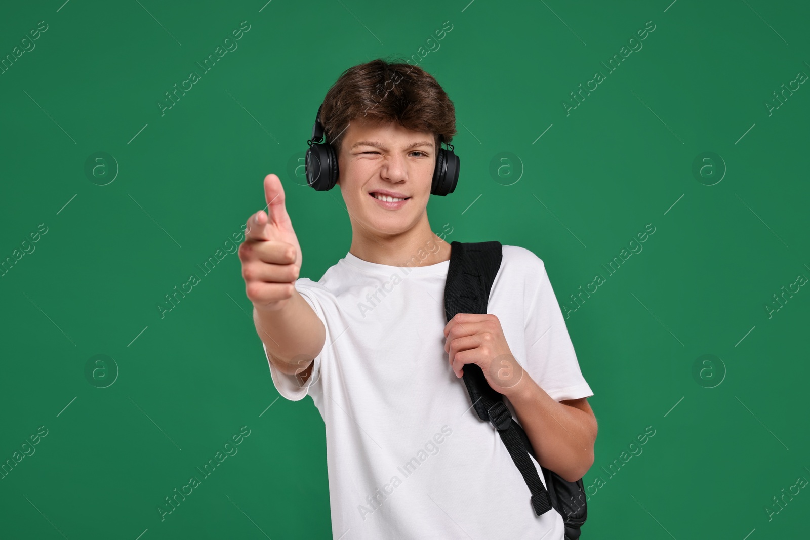 Photo of Teenage boy in headphones with backpack on green background