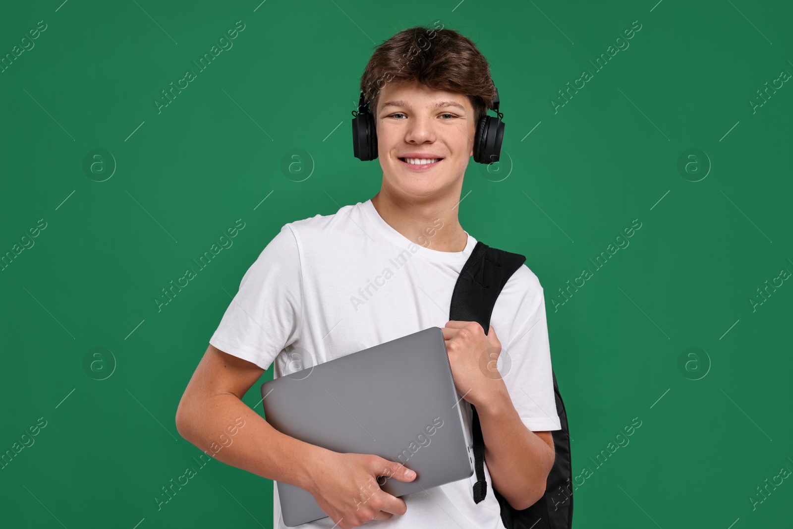 Photo of Teenage boy in headphones with laptop on green background