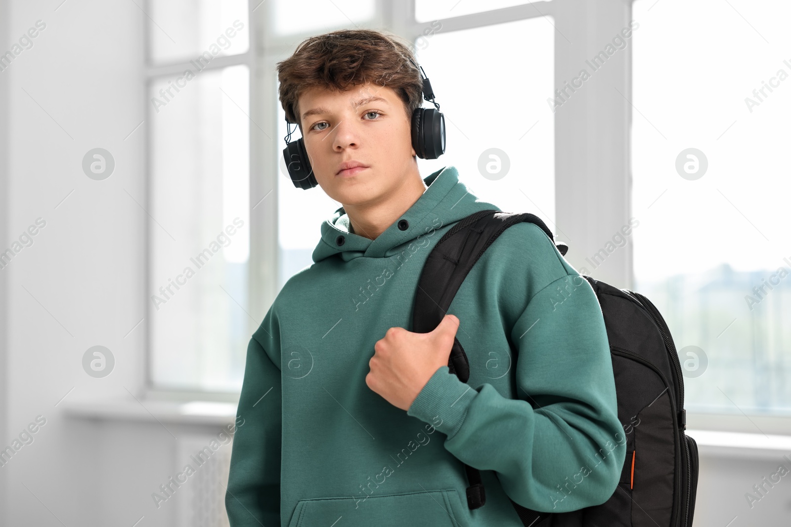 Photo of Teenage boy in headphones with backpack indoors