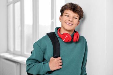 Photo of Happy teenage boy with headphones and backpack indoors