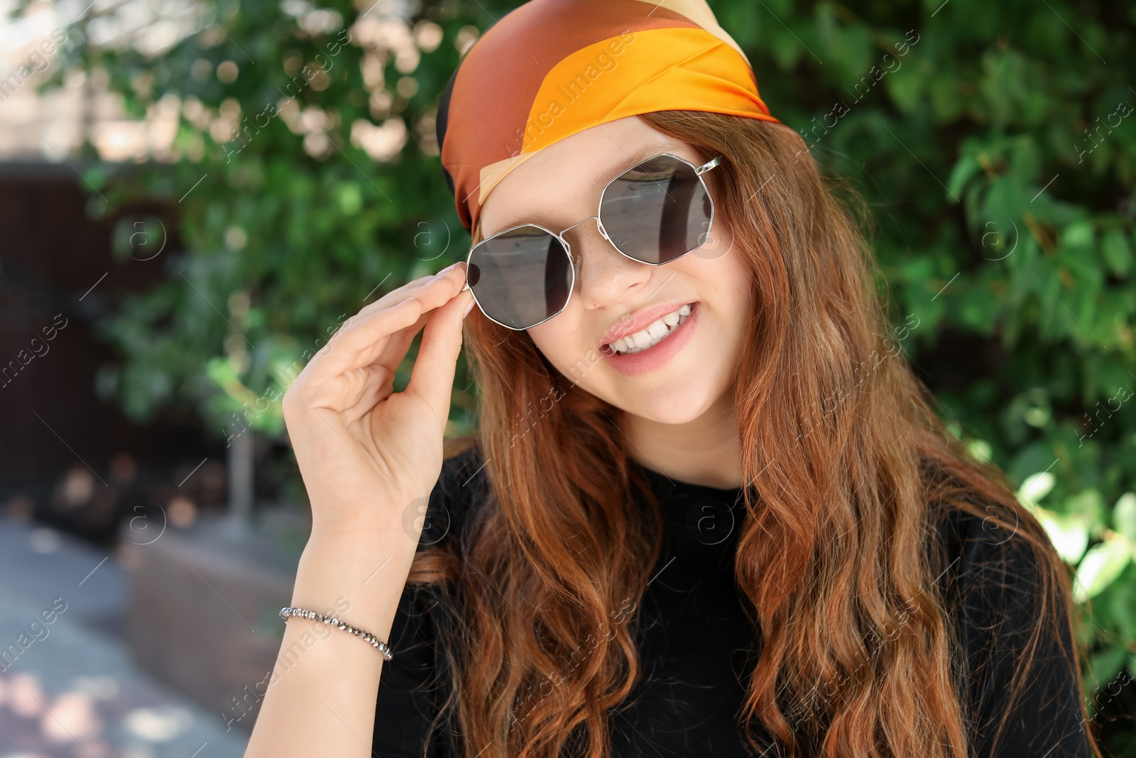 Photo of Portrait of happy teenage girl with long hair wearing sunglasses and bandana outdoors