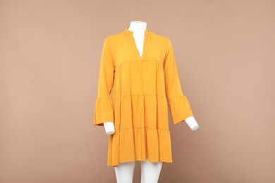 Female mannequin with stylish orange dress on beige background