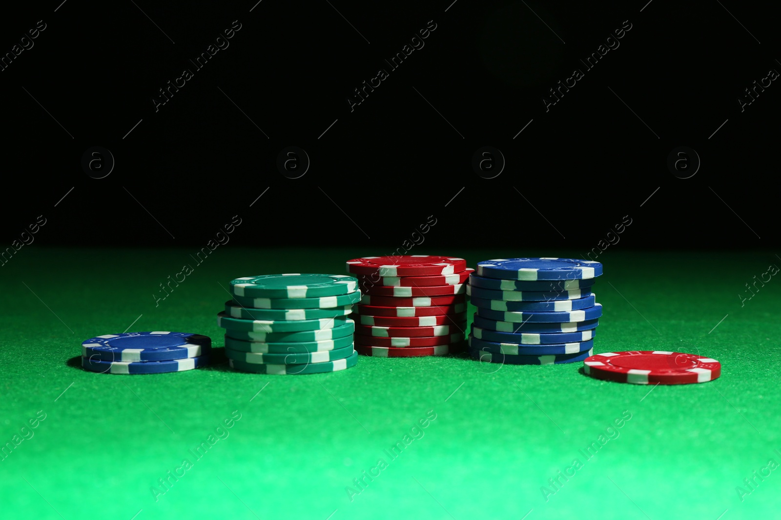 Photo of Poker chips on green table against dark background