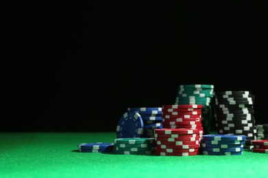 Photo of Poker chips on green table against dark background, space for text