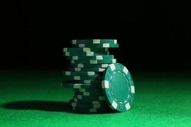 Stack of poker chips on green table against dark background, closeup