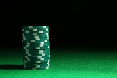 Photo of Stack of poker chips on green table against dark background, closeup. Space for text