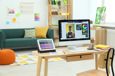 Photo of Designer's workplace with computer, tablet, color palette and stationery on wooden table indoors