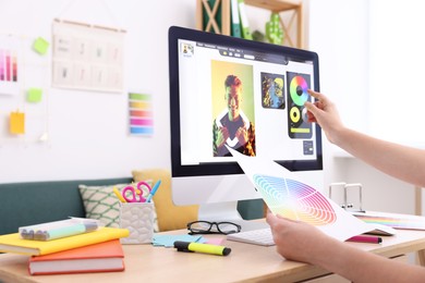 Photo of Designer with color palette working at wooden table indoors, closeup