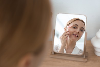 Photo of Smiling woman doing facial self massage with roller near mirror at home