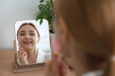 Photo of Smiling woman doing facial self massage with roller near mirror at home