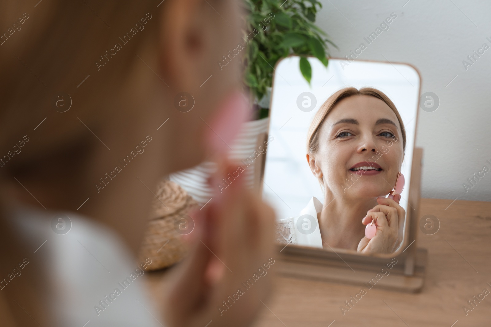 Photo of Smiling woman doing facial self massage with roller near mirror at home