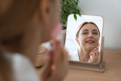 Photo of Smiling woman doing facial self massage with roller near mirror at home