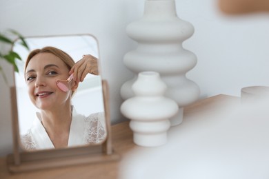 Photo of Smiling woman doing facial self massage with roller near mirror at home