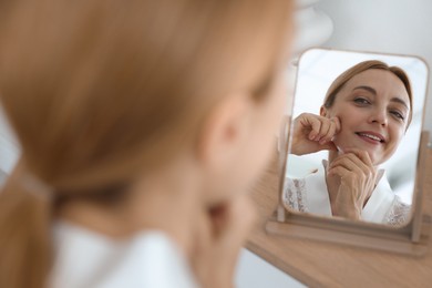 Photo of Smiling woman doing facial self massage near mirror at home