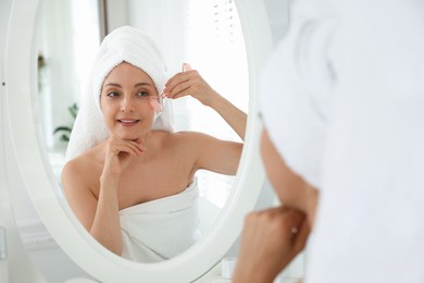 Smiling woman doing facial self massage with roller near mirror in bathroom