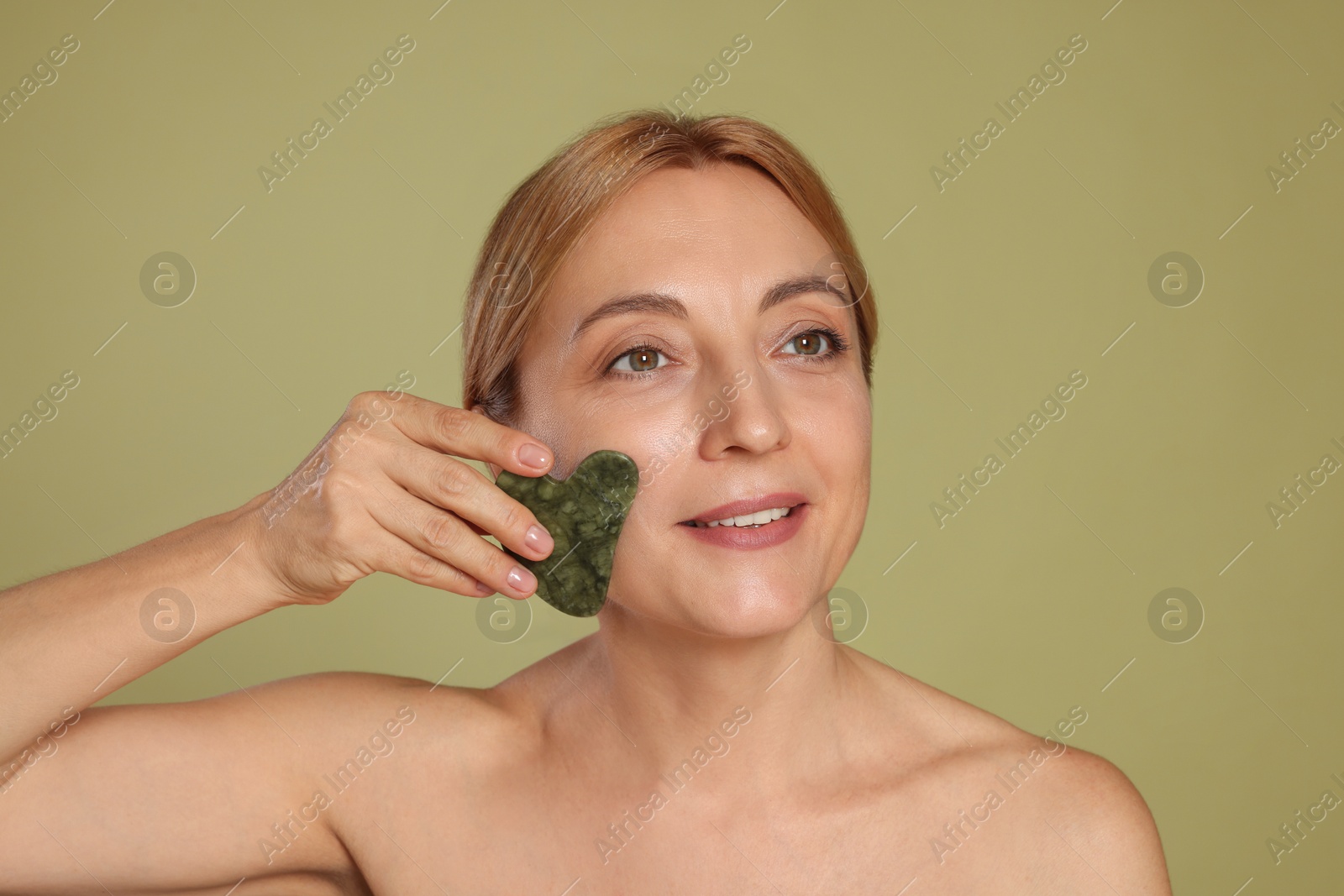 Photo of Smiling woman doing facial self massage with gua sha tool on green background