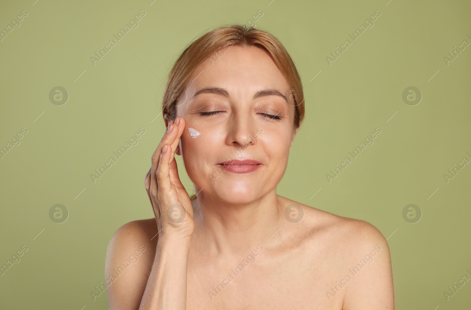 Photo of Beautiful woman with cream on face doing self massage against green background