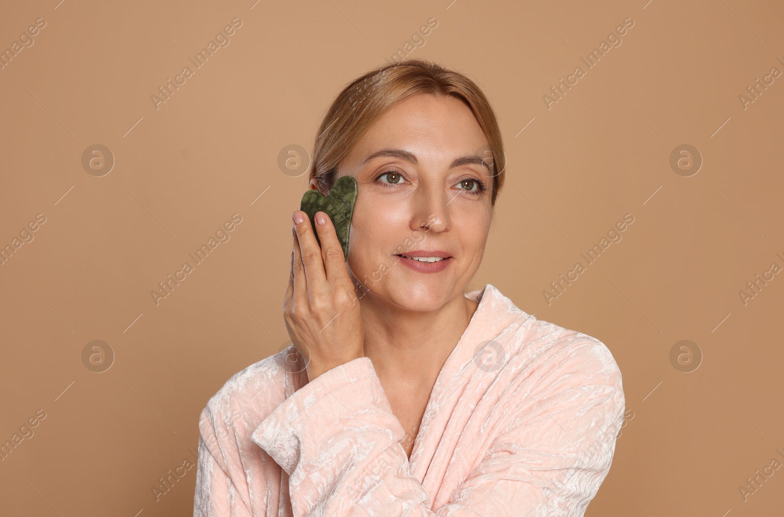 Photo of Smiling woman doing facial self massage with gua sha tool on beige background