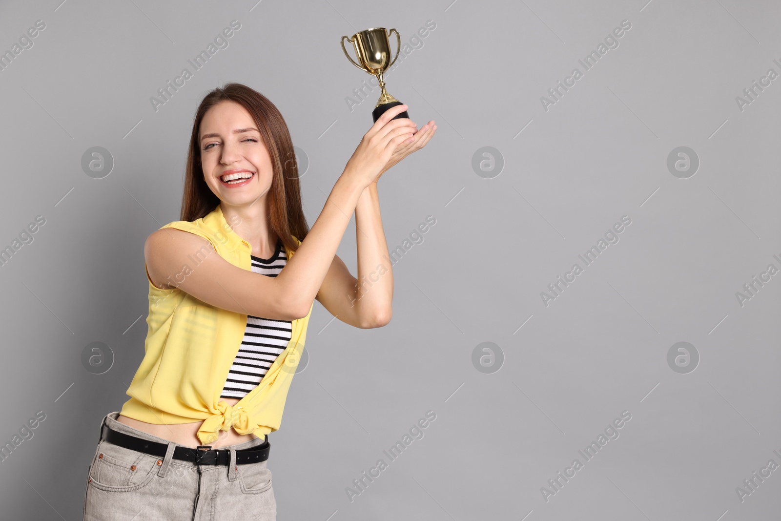 Photo of Happy winner with gold trophy cup on gray background, space for text