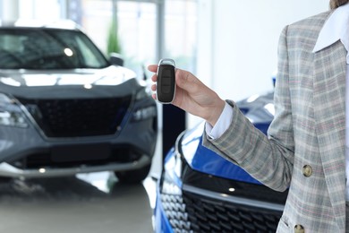 Saleswoman holding key near new car in salon, closeup