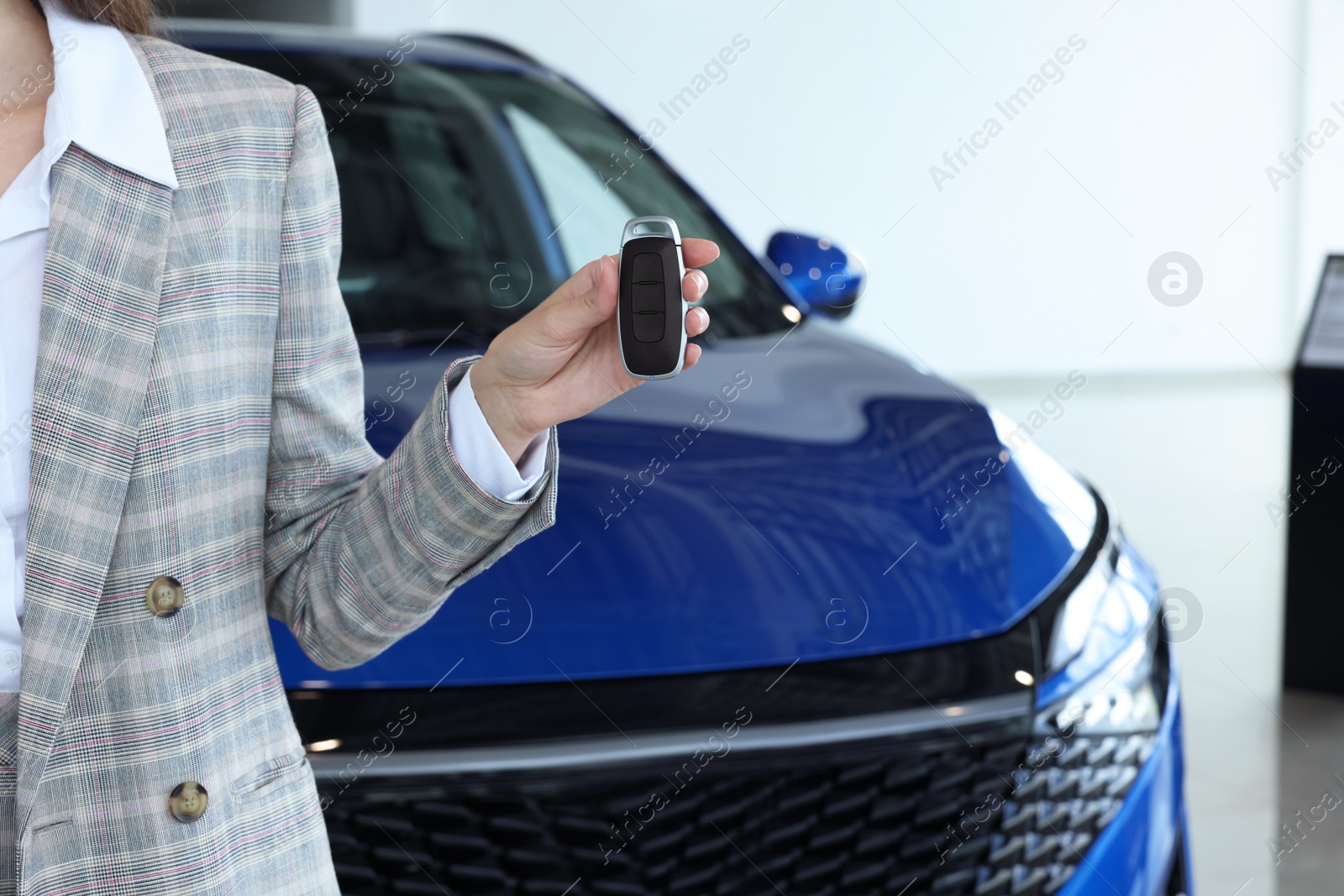 Photo of Saleswoman holding key near new car in salon, closeup