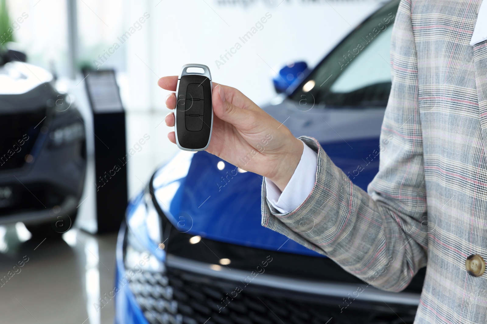 Photo of Saleswoman holding key near new car in salon, closeup