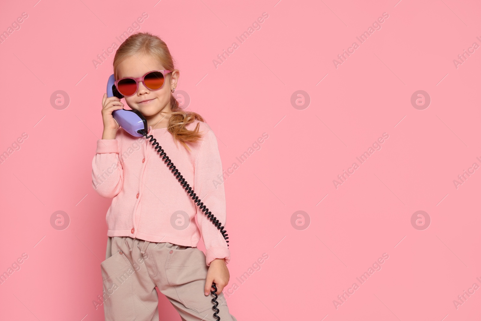 Photo of Cute little girl with handset of telephone on pink background, space for text