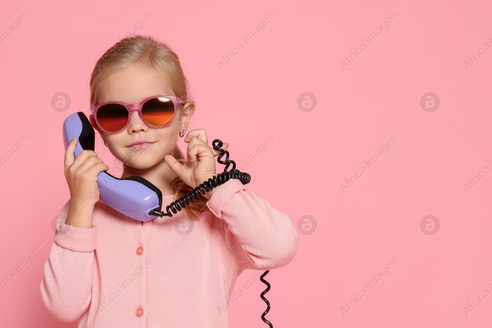 Photo of Cute little girl with handset of telephone on pink background, space for text