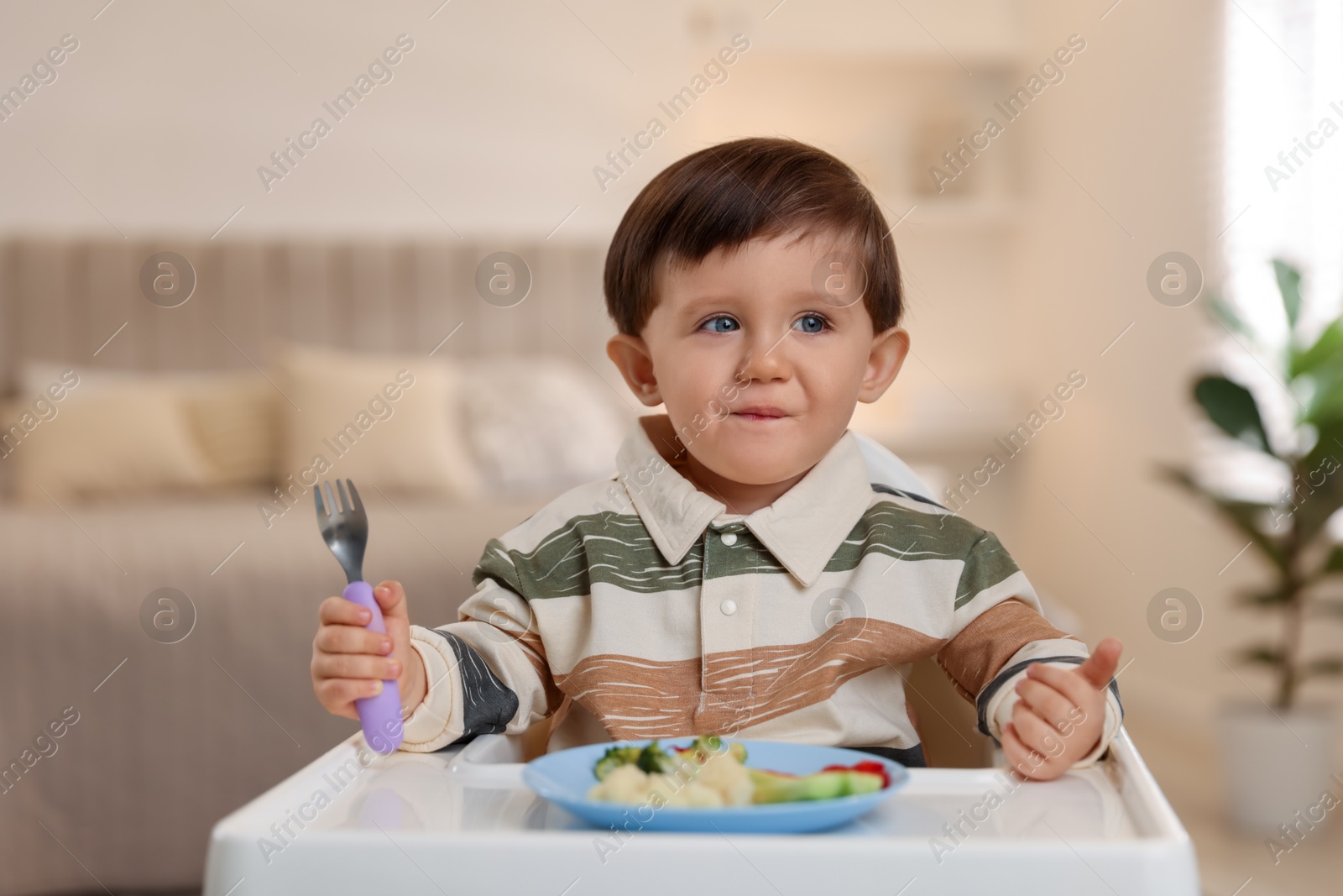 Photo of Cute little baby eating healthy food in high chair at home