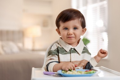 Photo of Cute little baby eating healthy food in high chair at home